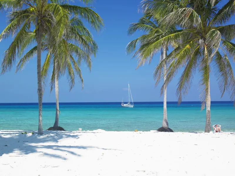 Palmy na białej plaży na Kubie, w tle jacht