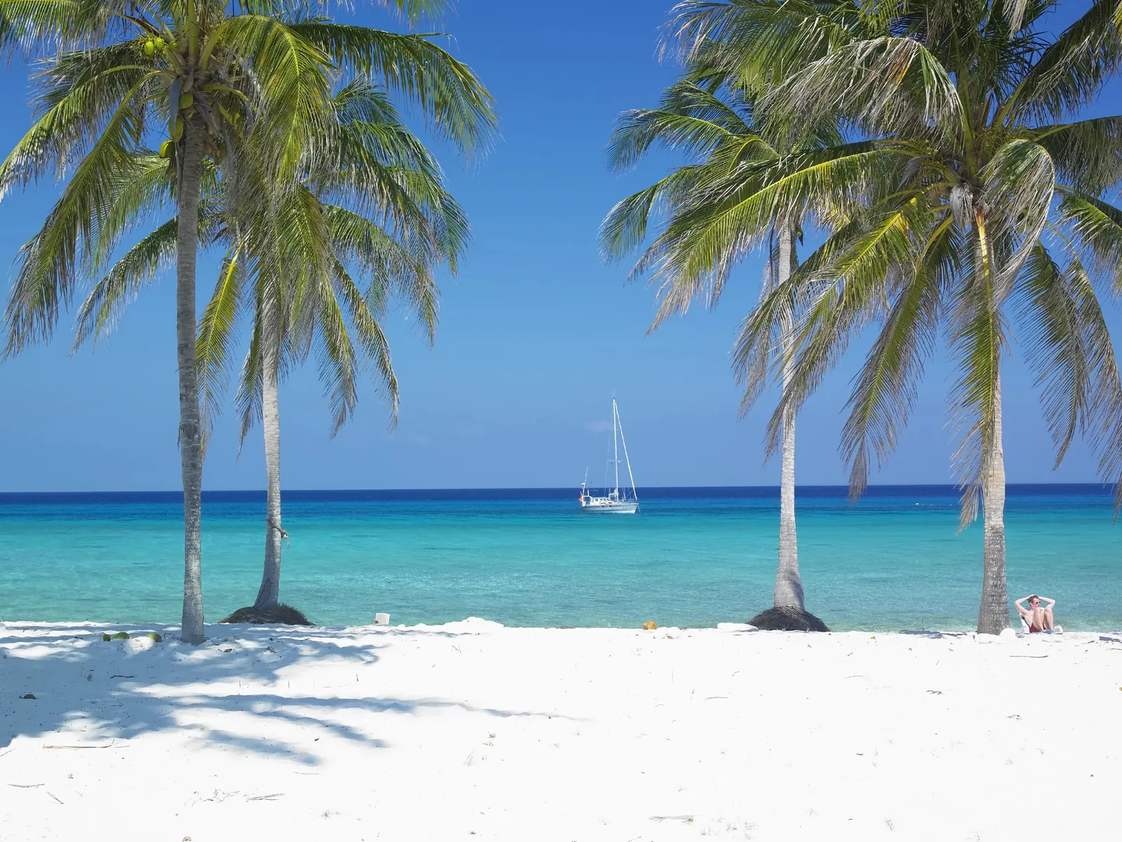 Palmy na białej plaży na Kubie, w tle jacht